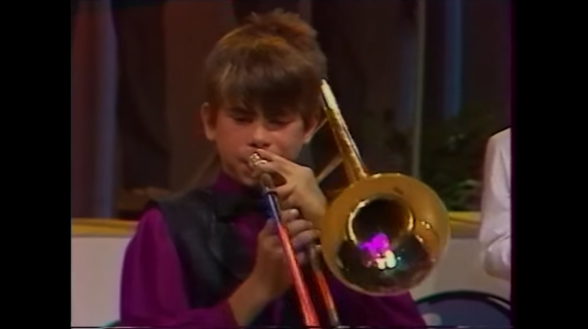 Raksta attēls - Maziņš Intars Busulis sandalēs pūš trombonu. 1991. gada ieraksts